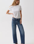 A woman modeling a white short-sleeve t-shirt and blue wide-leg jeans with black loafers, standing against a plain white studio background.