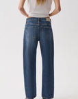 A model viewed from the back wearing a pair of wide-leg blue jeans, a white t-shirt, and black shoes, set against a plain light gray studio background.