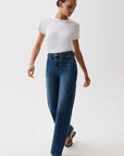A model wearing a white short-sleeve crewneck t-shirt, high-waisted wide-leg blue jeans with a gold-tone belt, and black heeled sandals, standing against a plain light gray studio background.