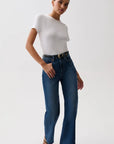 A model wearing a white short-sleeve crewneck t-shirt, high-waisted wide-leg blue jeans with a gold-tone belt, and black heeled sandals, standing against a plain light gray studio background.