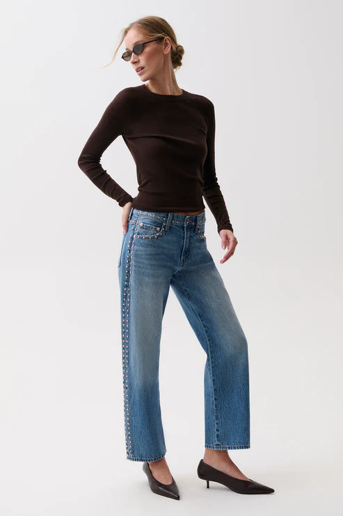 Woman wearing a black long-sleeve top and blue jeans on a white background