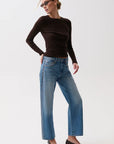 Woman wearing a black long-sleeve top and blue jeans on a white background