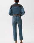 A model shown from the back wearing a cropped denim jacket with dark gray shoulder panels and blue denim body, paired with blue jeans and black heels, against a plain white studio background.