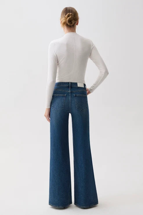 A model shown from the back wearing a white long-sleeve mock-neck top and high-waisted, wide-leg blue denim jeans against a plain white studio background.