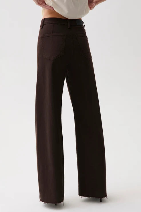 A person wearing dark brown wide-leg trousers with a white top, shown from the waist down against a light gray studio background.