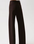 A person wearing dark brown wide-leg trousers with a white top, shown from the waist down against a light gray studio background.
