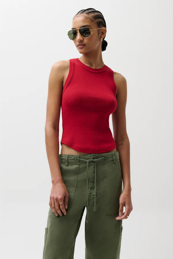 Woman wearing a red sleeveless top and green pants against a white background