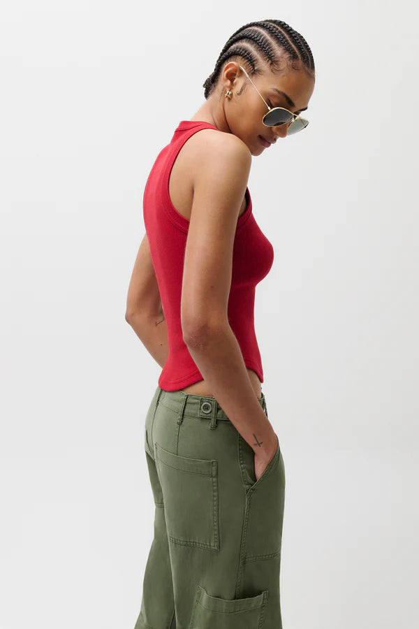 Woman wearing a red sleeveless top and green cargo pants against a white background