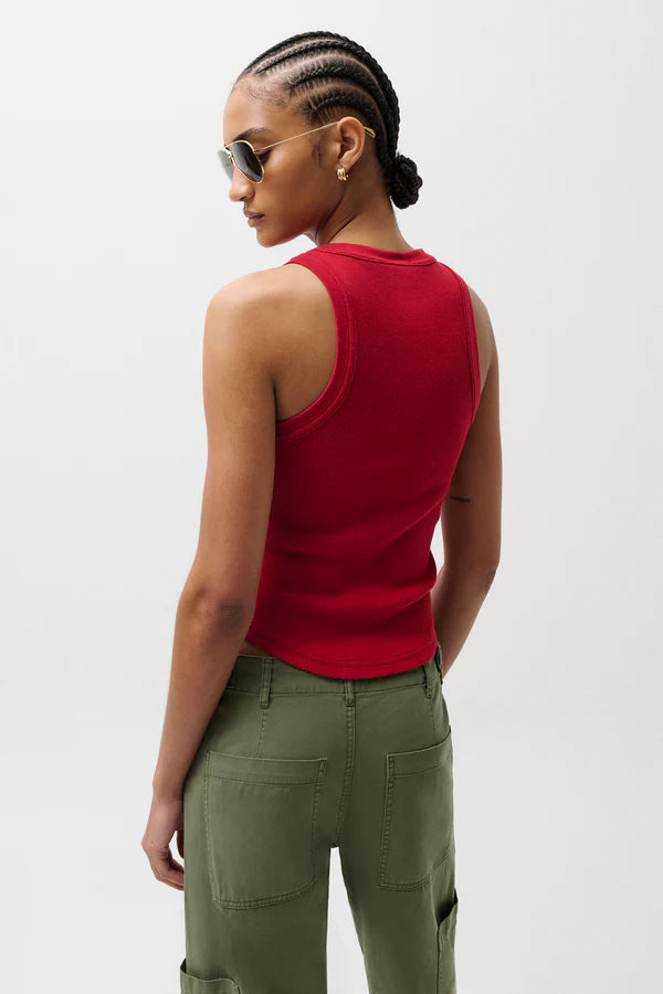 Woman wearing a red sleeveless top and green pants against a white background