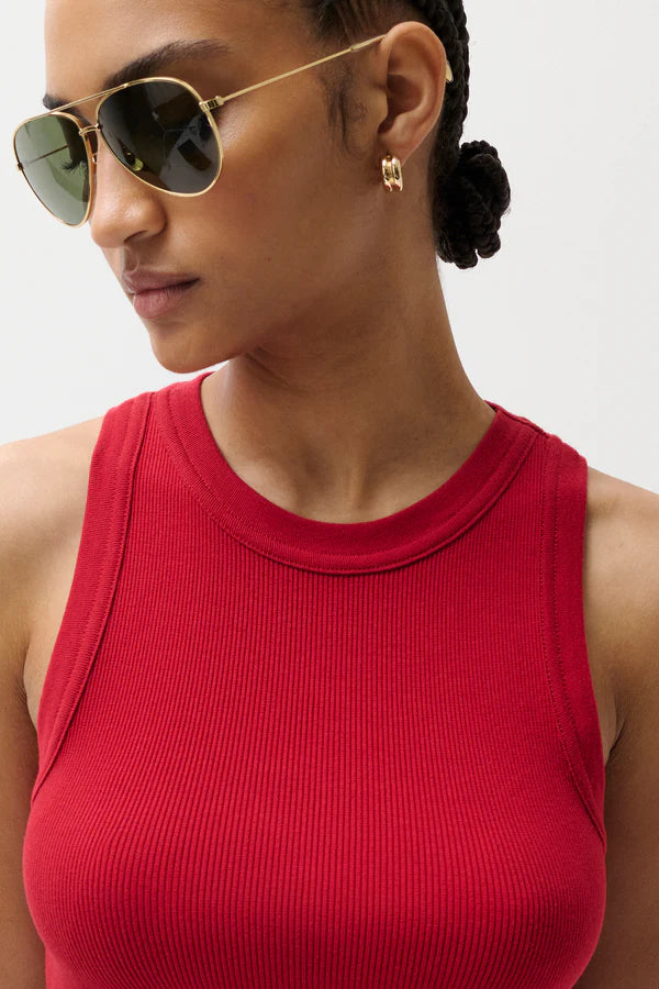 Woman wearing a red tank top and gold sunglasses with a neutral background
