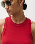 Woman wearing a red tank top and gold sunglasses with a neutral background