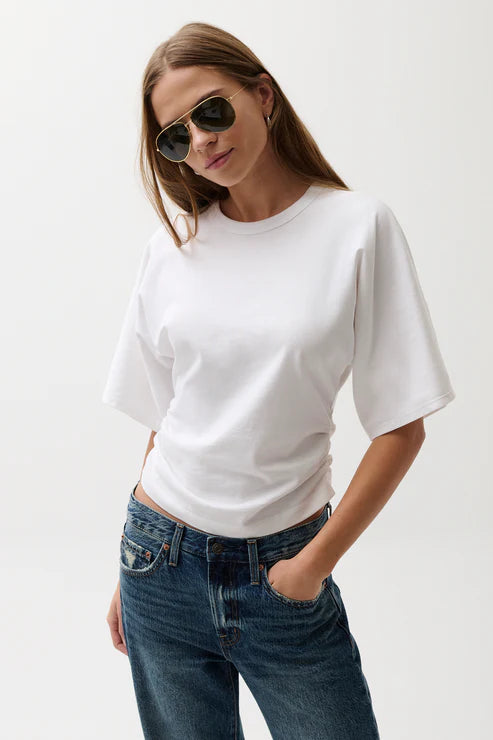 Woman wearing a white t-shirt and blue jeans against a plain background