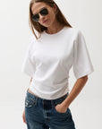 Woman wearing a white t-shirt and blue jeans against a plain background