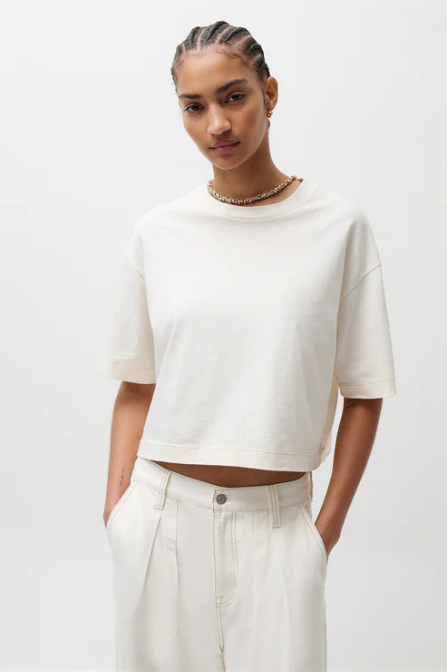 Person wearing a white crop top and light-colored pants on a plain background