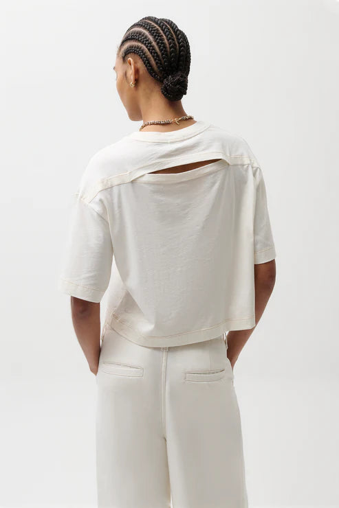 Person wearing a white outfit with a cut-out design on a plain background, back