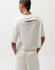 Person wearing a white outfit with a cut-out design on a plain background, back