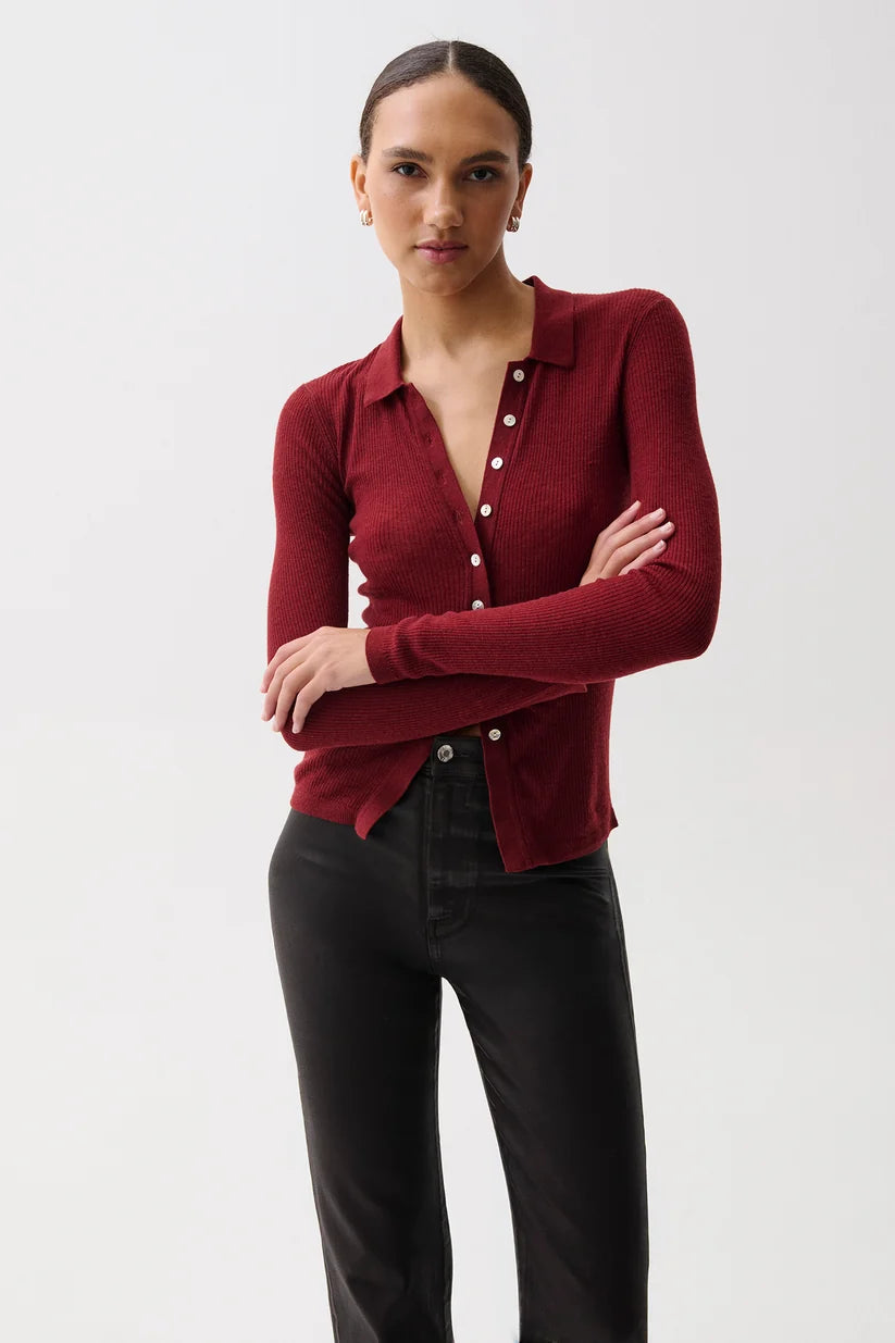 A woman modeling a fitted long-sleeve knit polo-style cardigan in deep burgundy with white buttons, paired with black pants, against a plain light gray studio background.