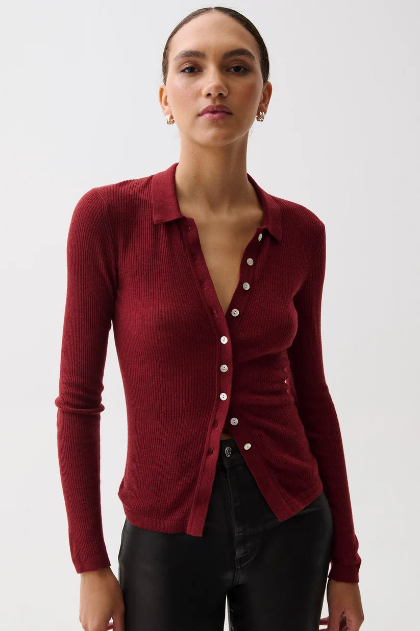 A woman modeling a ribbed long-sleeve button-front cardigan in deep burgundy red, paired with black pants, against a plain light gray studio background.