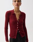 A woman modeling a ribbed long-sleeve button-front cardigan in deep burgundy red, paired with black pants, against a plain light gray studio background.