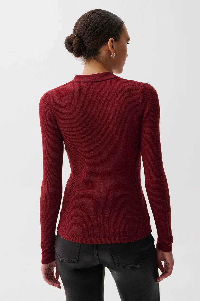 A woman shown from the back wearing a fitted long-sleeve ribbed knit top in deep burgundy red, paired with black pants, against a plain light gray studio background.
