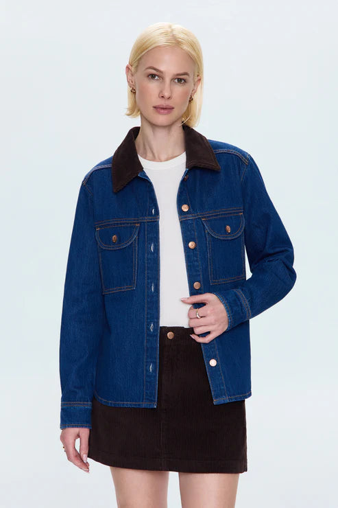 Woman wearing a blue denim jacket with a white shirt and black skirt on a light gray background