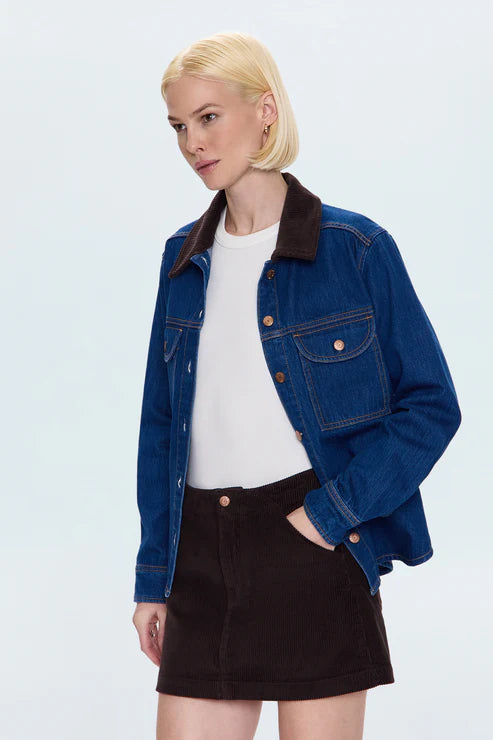 Woman wearing a blue denim jacket over a white shirt and black skirt on a light blue background, front/side view