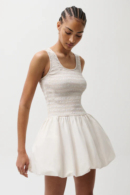 Woman wearing a white dress with a textured bodice on a plain background