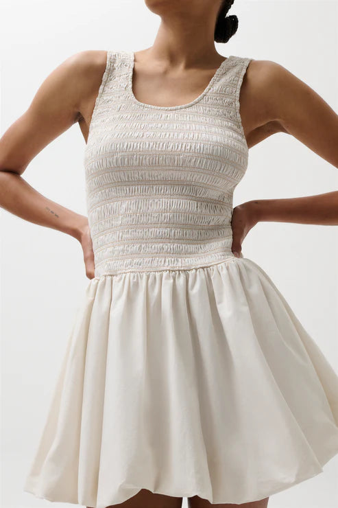 Woman wearing a white dress with a textured bodice on a plain background