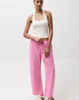 Woman wearing a white tank top and pink pants on a white background