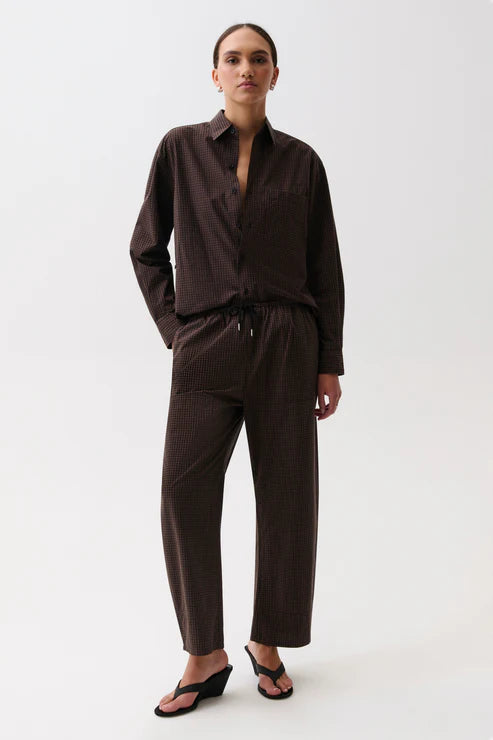 A model wearing a dark brown long-sleeve button-up shirt and matching dark brown wide-leg pants with a drawstring waist, paired with black wedge sandals, against a plain white studio background.