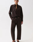 A model wearing a dark brown long-sleeve button-up shirt and matching dark brown wide-leg pants with a drawstring waist, paired with black wedge sandals, against a plain white studio background.