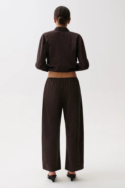 A model viewed from the back wearing a dark brown cropped long-sleeve shirt and matching wide-leg trousers, paired with black pointed-toe heels, against a plain light gray studio background.