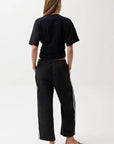 Person wearing a black t-shirt and black pants with white stripes on a white background