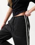 Person wearing black pants with a white stripe on a light background