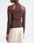 A model shown from the back wearing a ribbed long-sleeve mock neck top with shoulder cutouts in a dark brown color, paired with cream pleated trousers, against a plain white background.