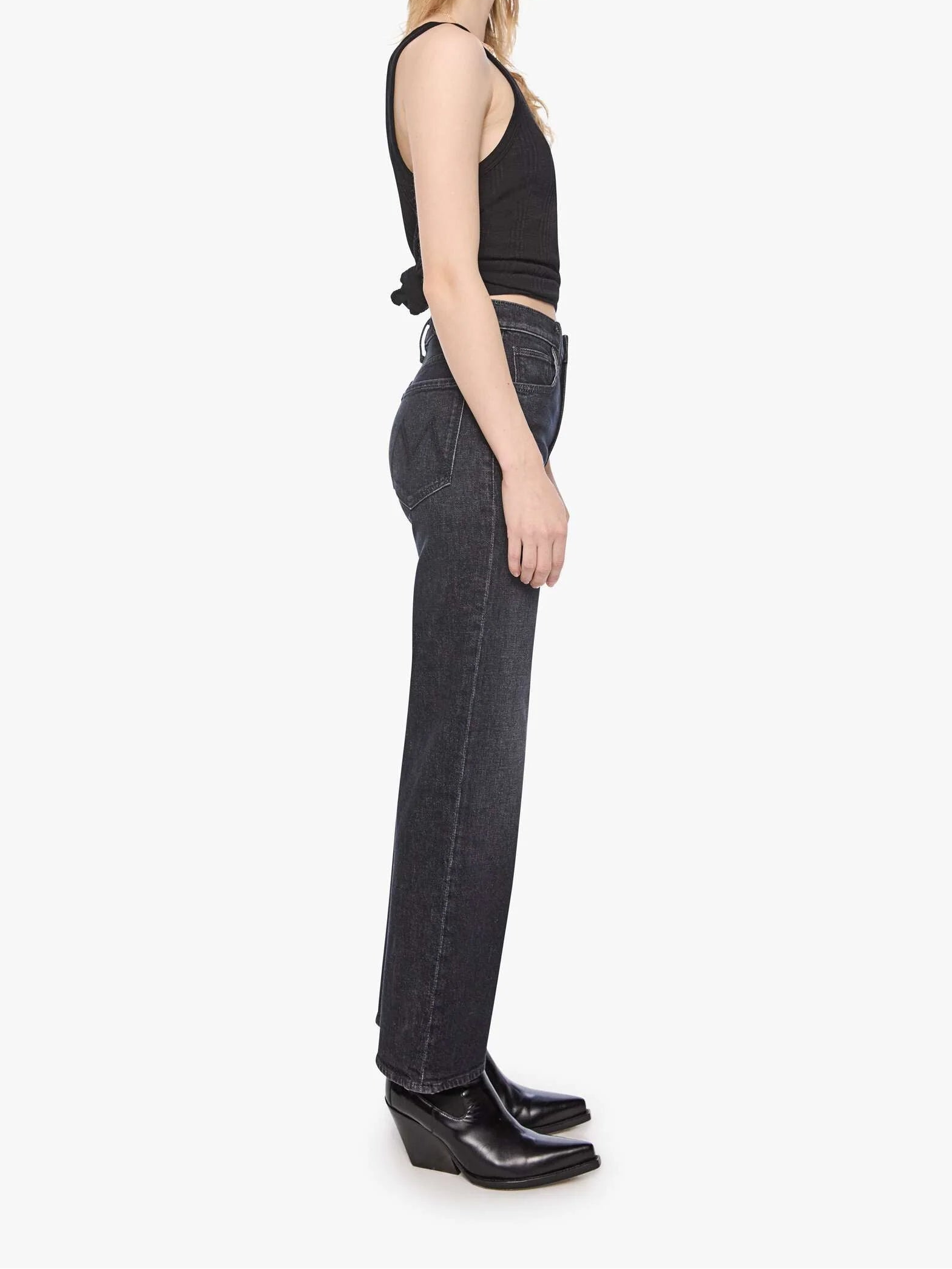 Woman wearing black tank top and dark jeans standing against a white background