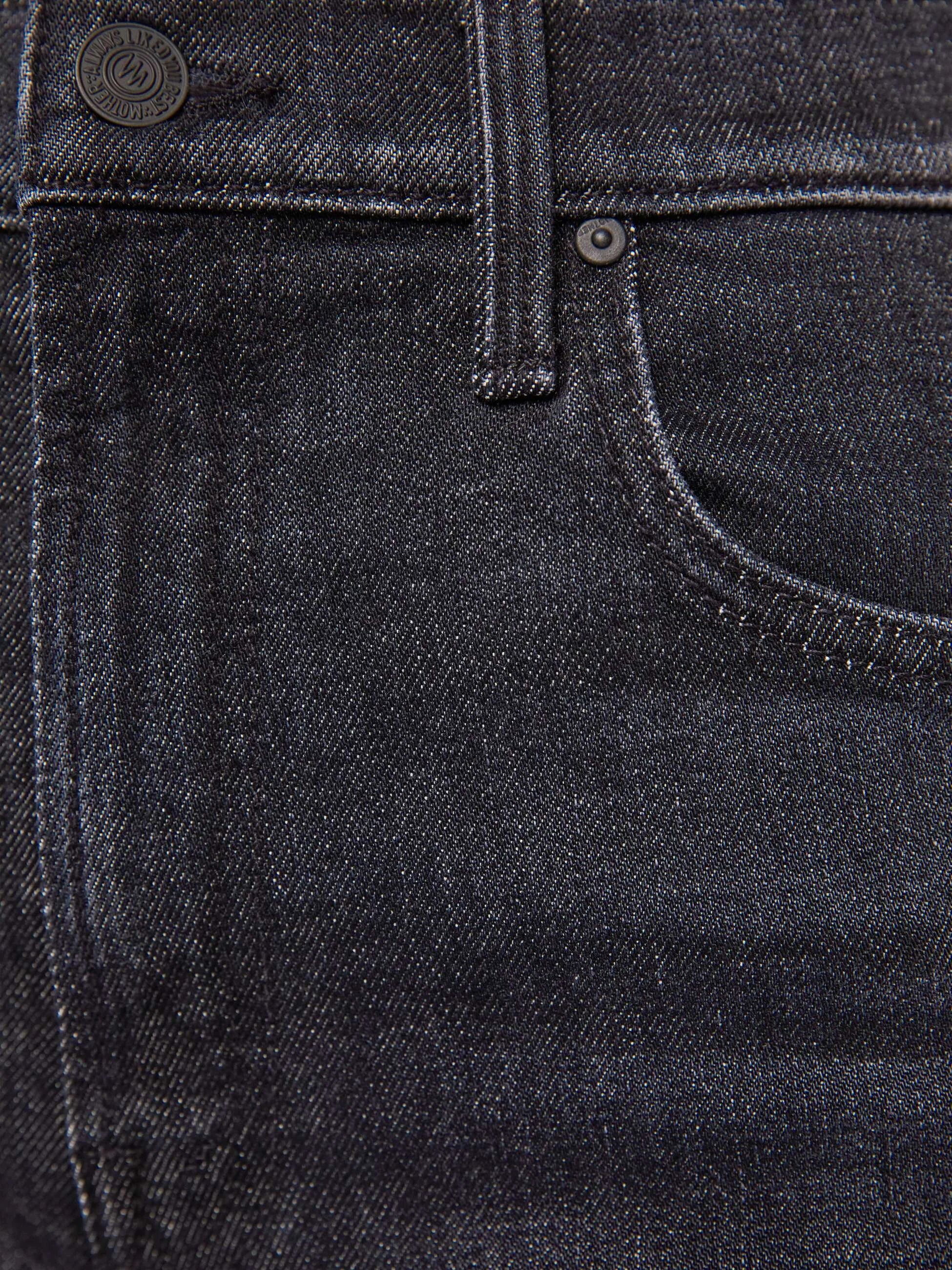 Close-up of dark washed denim jeans showing the waistband, button, belt loop, front pocket, and fabric texture.
