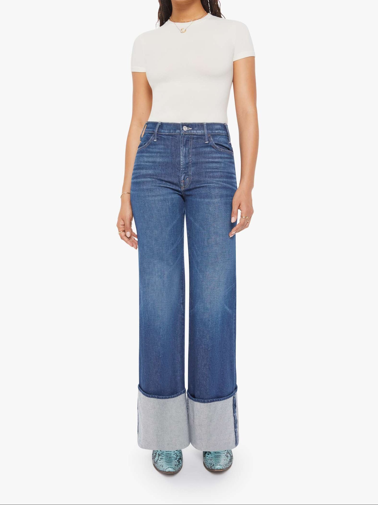 Woman wearing blue cuffed jeans and a white top on a white background, front