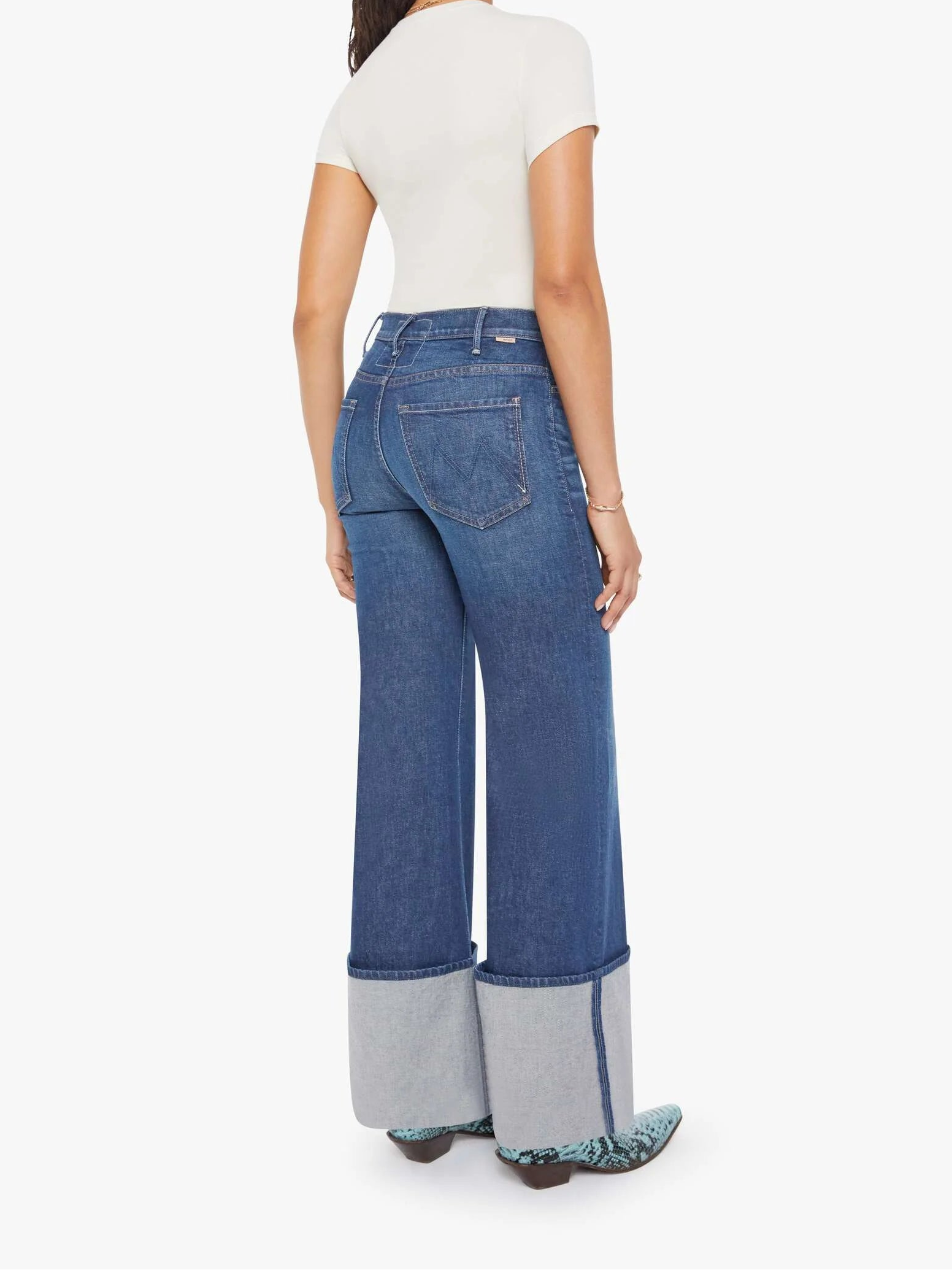 Woman wearing blue cuffed jeans with a white background, back