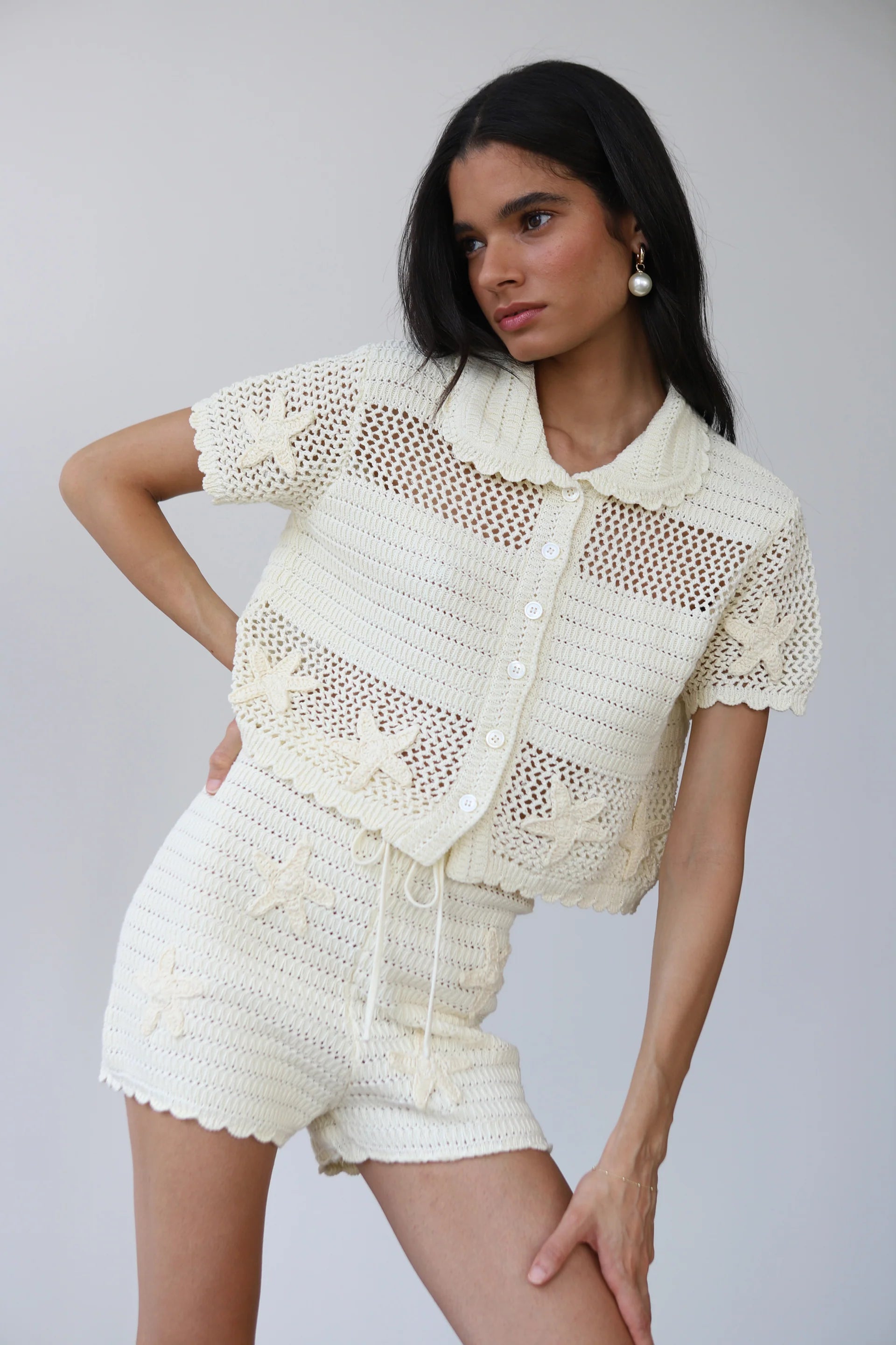 Woman wearing a cream-colored crochet outfit on a plain background