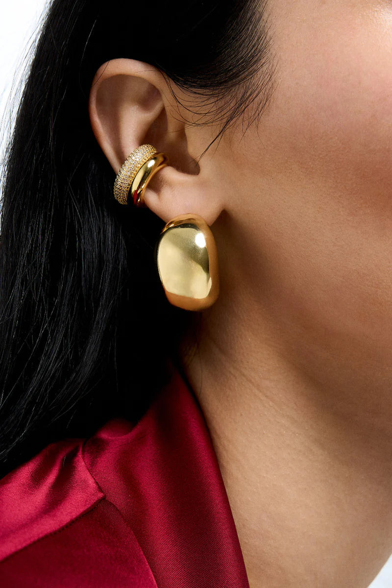 Close-up of a person wearing gold earrings with a blurred background