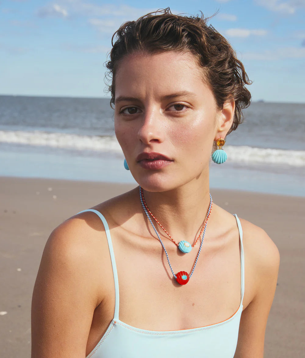 Woman on a beach wearing turquoise earrings and layered necklaces