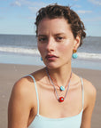 Woman on a beach wearing turquoise earrings and layered necklaces