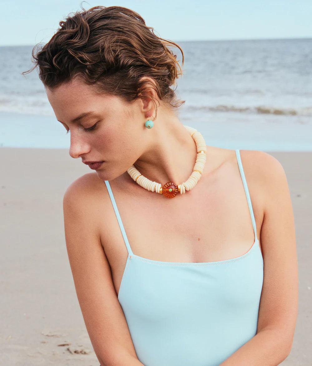 Woman wearing a light blue top and a necklace with a beach background