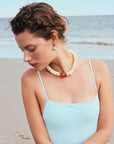 Woman wearing a light blue top and a necklace with a beach background