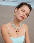 Woman on a beach wearing a light blue necklace with colorful pendants