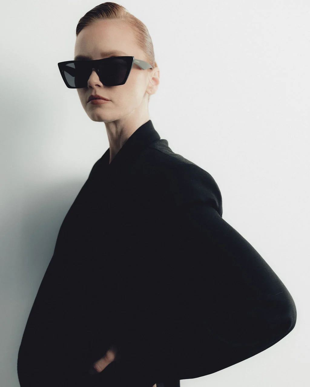 Person wearing a black outfit and sunglasses on a plain background