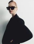 Person wearing a black outfit and sunglasses on a plain background