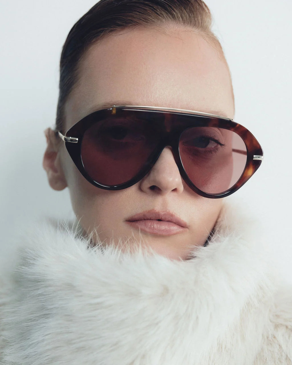 model wearing tortoise sunglasses with gold accents and light red lenses on a grey background 
