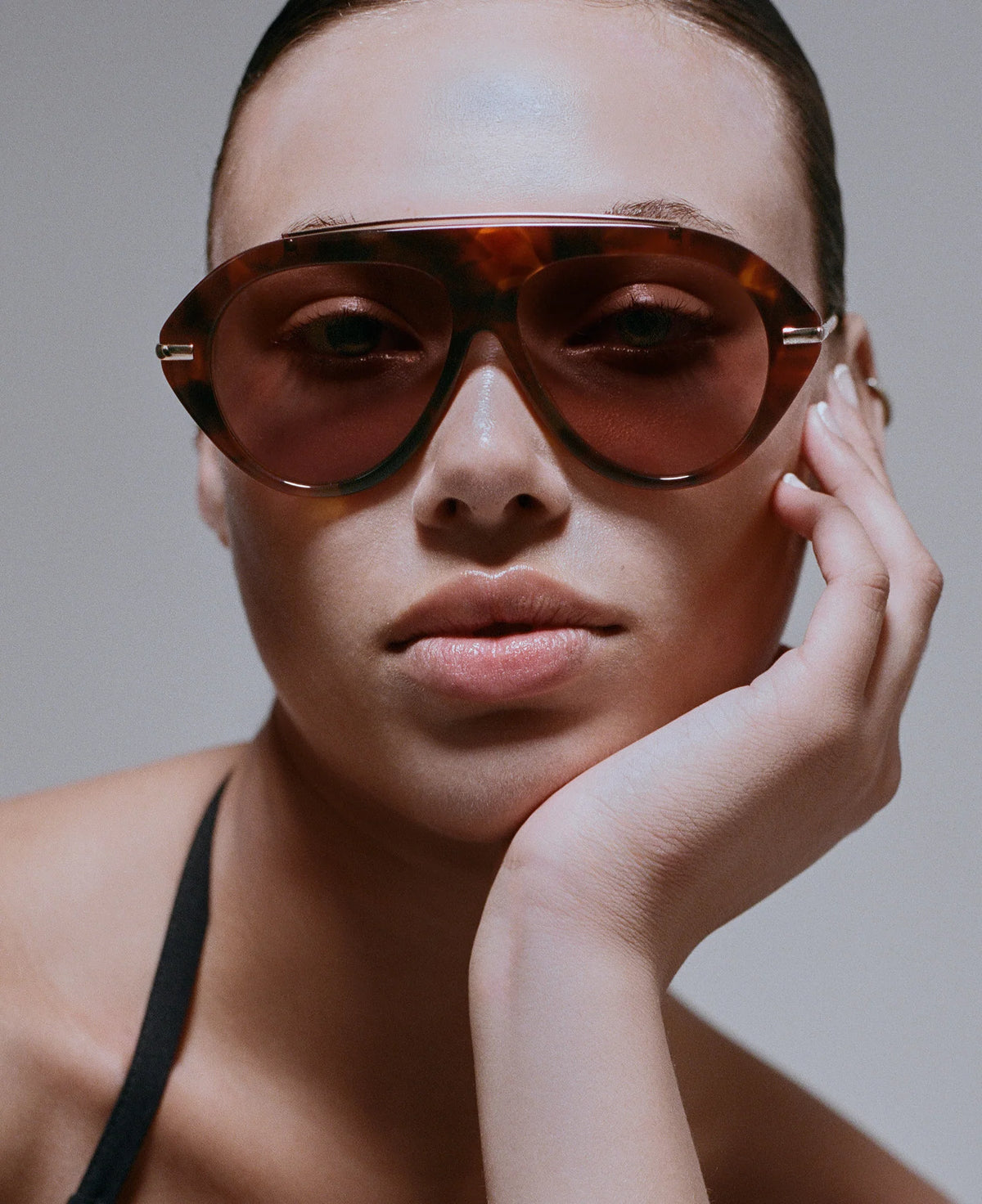 model wearing tortoise sunglasses with gold accents on a grey background 